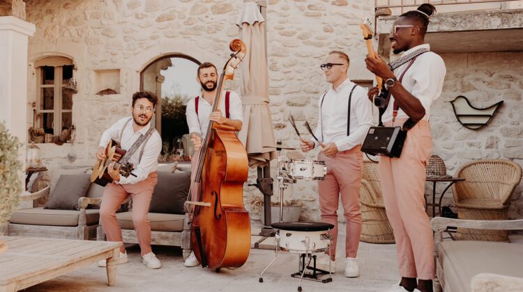 Un groupe de musiciens, Les Garçons Chics, portant des pantalons roses, joue des instruments ensemble.