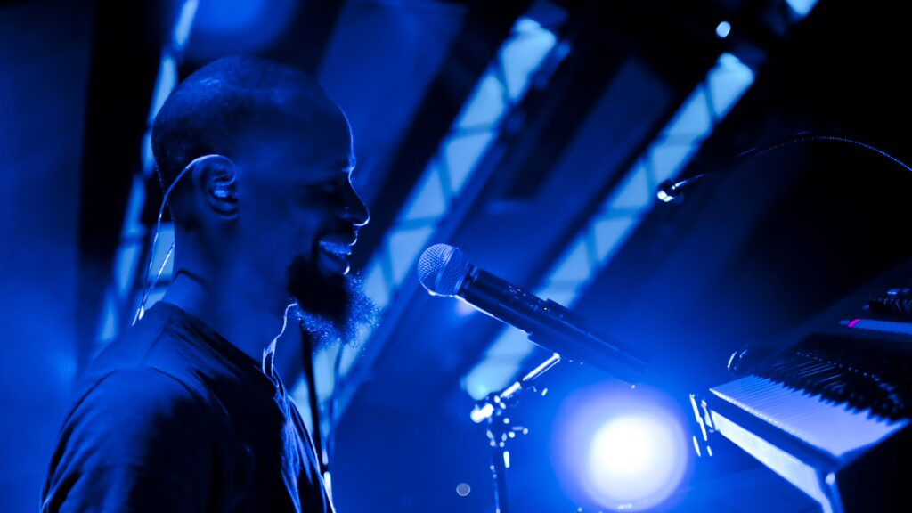 Expert en Booking d'Artistes et Production Événementielle 7 musicien et chanteur sur scène devant son micro et son piano sous une lumière bleue